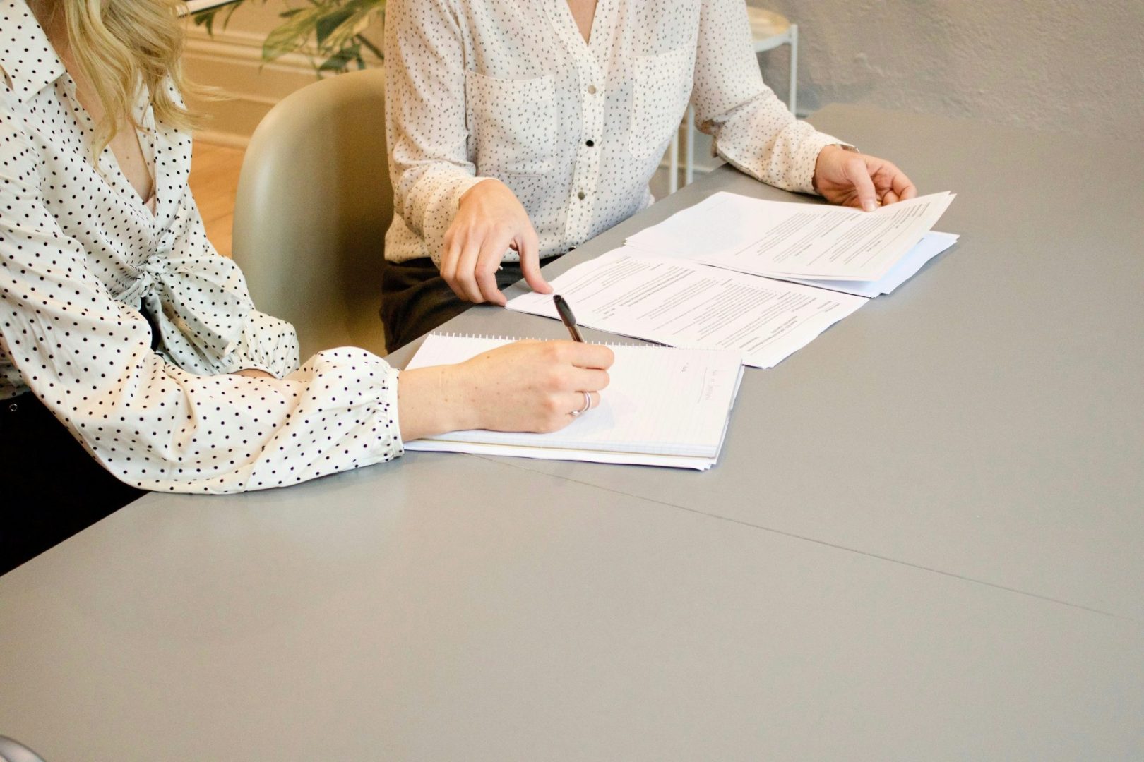 Une femme signe sur une feuille de papier blanc pour imprimante, à côté d'une femme sur le point de toucher les documents
